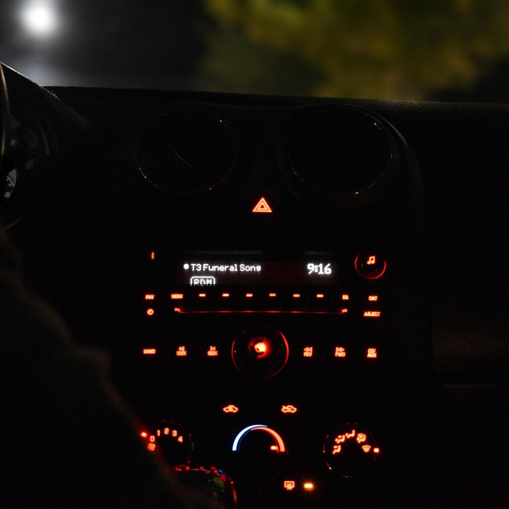 Picture of a car dashboard with a radio that reads "Funeral Song"